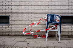 Stacked plastic chairs wrapped in barrier tape, that's blowing in the wind, a brick wall in the background