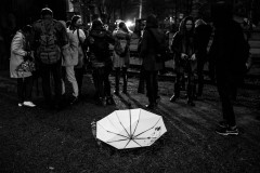 White, open umbrella, upside-down on dark ground, group of people in the background