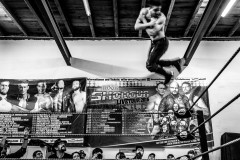 A wrestler, doing a cork screw from the top turnbuckle, mid-air, spectators around the ring, watching in awe