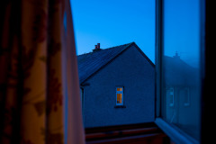 Singular, warmly lit window on a house during the blue hour
