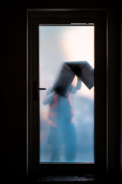 A man, wearing a high-visibility vest, seen through a frosted glas door