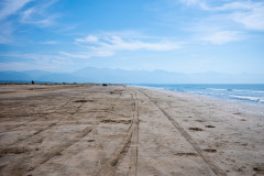At the beack, tire marks in the sand, bright blue sky above