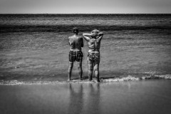 Old couple in their bathing suits, standing on the beach with their feet in the ocean