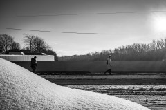 Snow covered car in the foreground, two figures walking across a bridge in the background