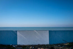 A small blut/white striped wall prevents direct access to the ocan, with a red cargo ship way off in the distance