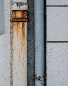 A rusty drain pipe running along side a non-rusty drain pipe