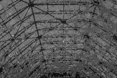 The frame of an old cooling tower is seen reflected in a dirty puddle of water