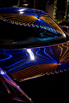 An illuminated ferris wheel is reflected on a cars windshield and hood