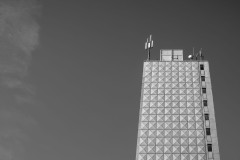 Monochrome photograph of a white, highrise building with some antennas on the roof against a clear