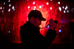 Sven, in profile, taking a photograph, with a crimson background
