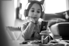 Monochrome image of my daugther (out of focus in the background) listening to music over headphones from her iPad (in focus in the foreground)