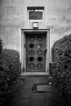Entryway framed by bushes on either side with a wodden door with two vertical lines of five hexagonal windows