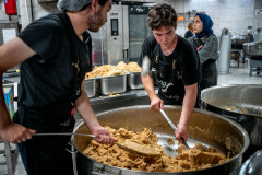 Volunteers empty a large pot full of irmik helvasi (a semolina dessert).