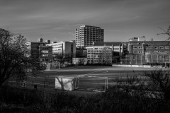Football pitch draped in long shadows with buildings in the background
