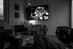 Doc Brown seen on the screen of a wall-mounted tv, crosed legs of the viewers in the foreground