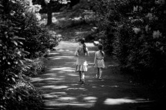 Monochromatic photograph of my two daughters walking on a shadowy path flanked by trees