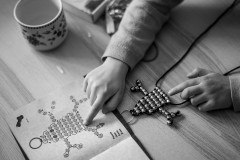 My daugher is pointing to the instructions, while threading pearls to create a frog