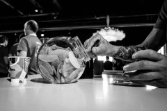 Close-up of a tattooed hand reaching into a glass jar filled with gummy candies